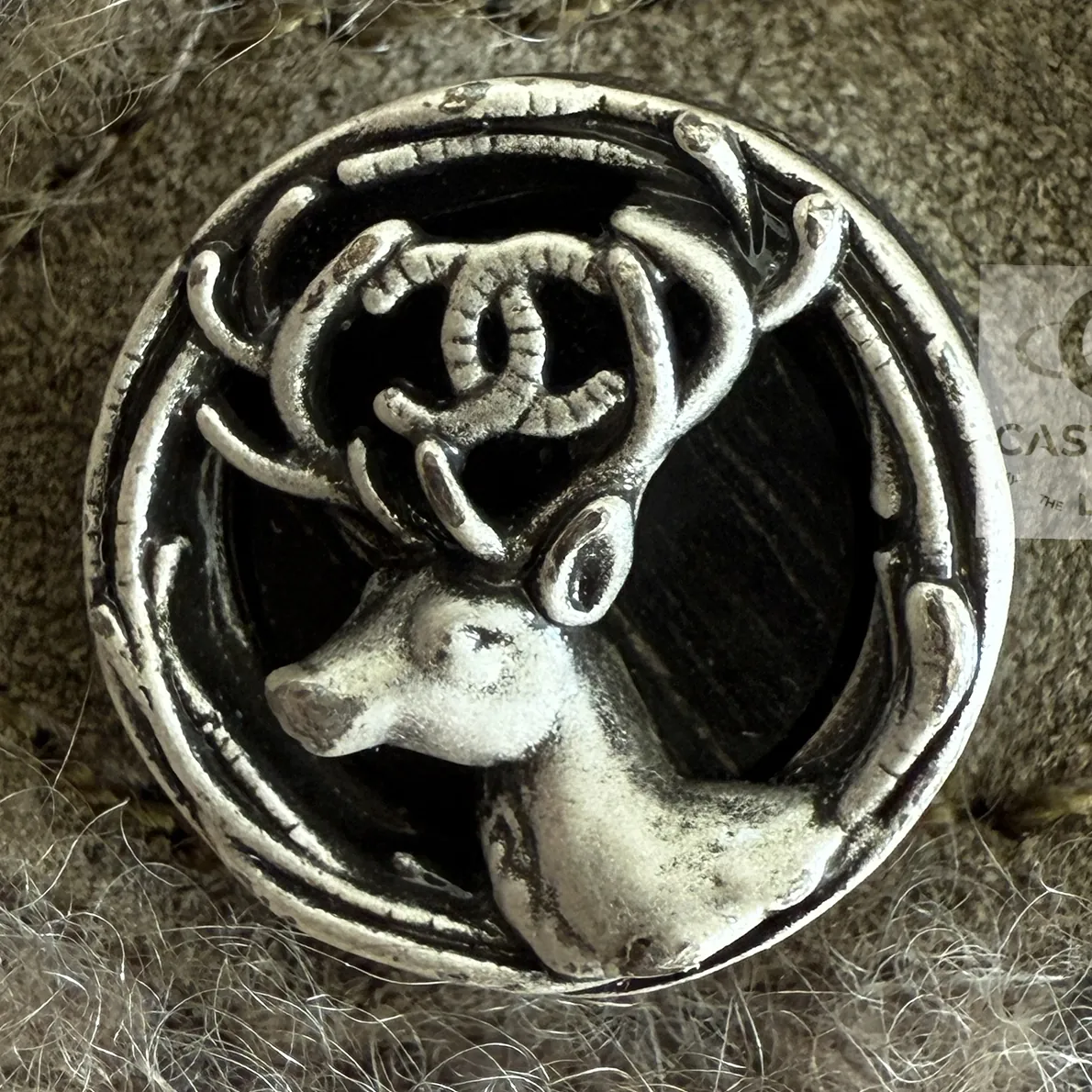 A silver-tone button on the cashmere jacket: a stag's head in a ring, the interlaced CC between its antlers
