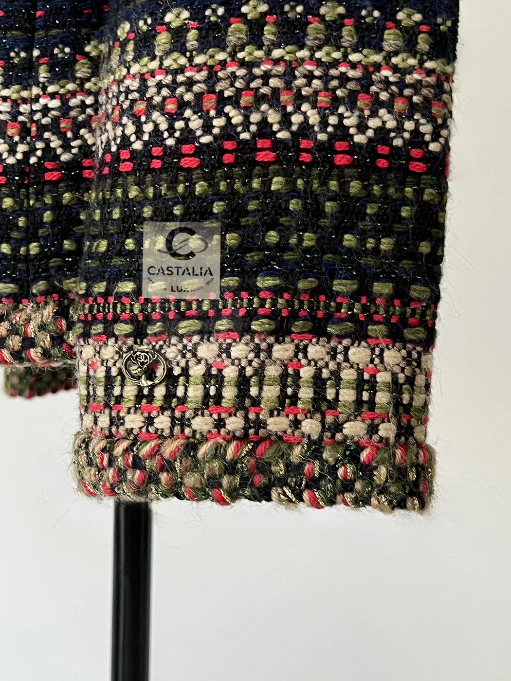A sleeve end: tweed bands, the braided cuff, and a small gilt stag-head charm hanging just above it