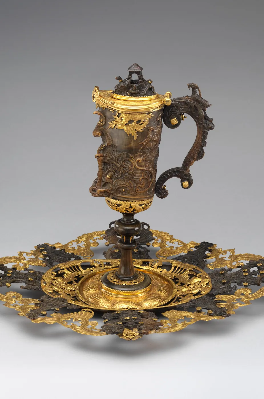A ewer of dark carved ibex horn with gilded mounts, on a gold openwork stand
